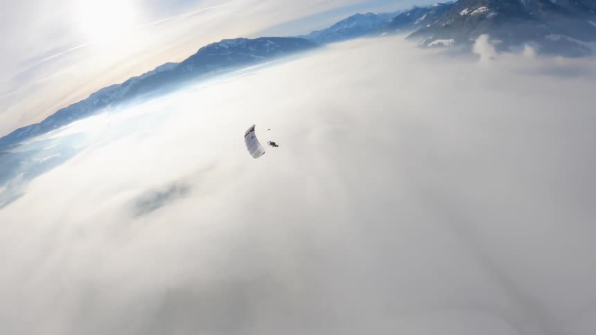 A person paragliding with a snow covered mountain range the sky and clouds in the background