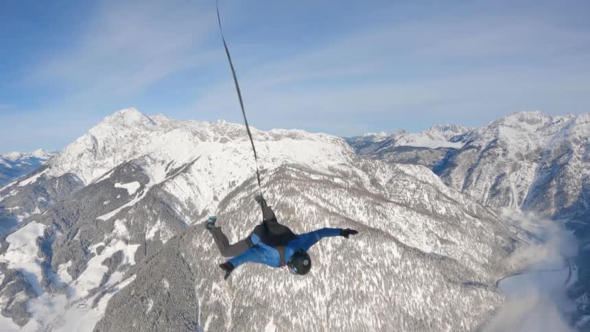 Skydiver opens parachute and moves higher into the sky above snow covered mountains