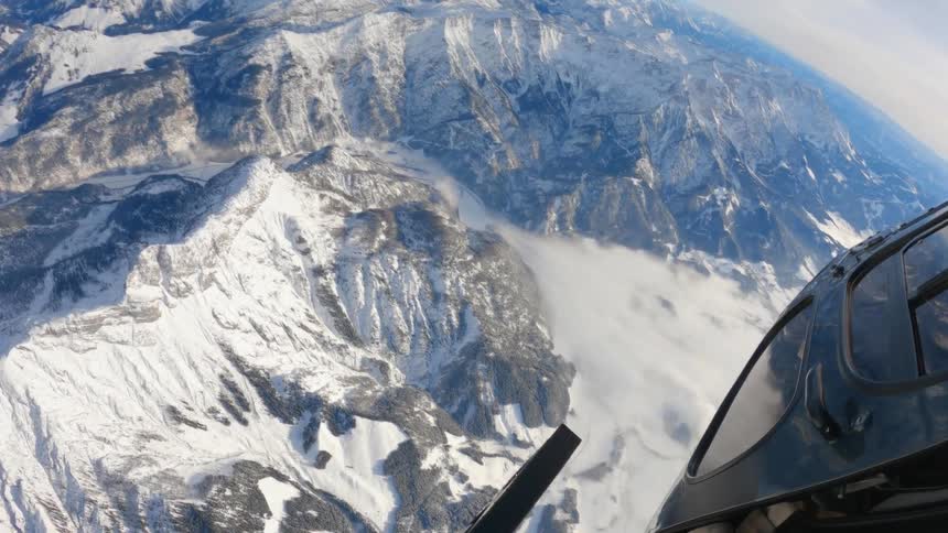 Leaning out the open door of a helicopter over snow covered mountains