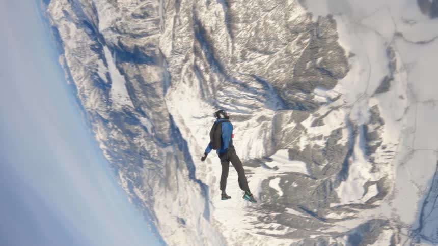 Aerial footage of a skydiver falling over the snow covered peaks of a mountain range