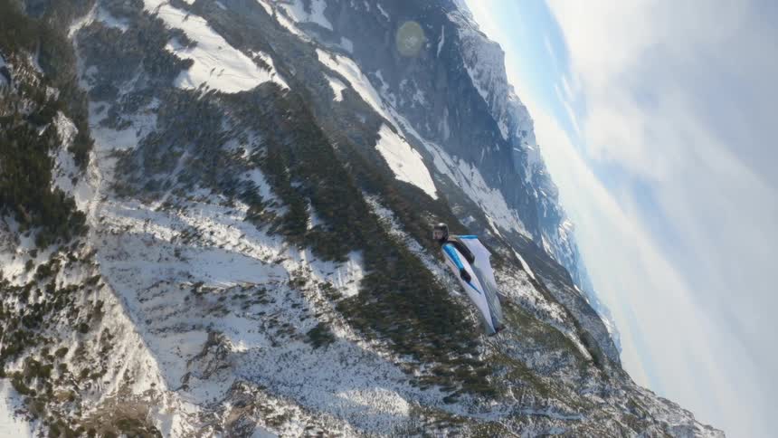 A person wingsuit flying over mountains and forests in the winter