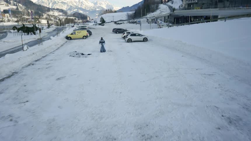Flying a drone over a parking lot full of snow towards a person