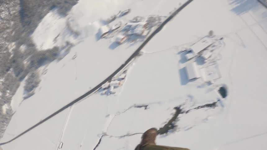A man parachutes down towards buildings on a snowy mountain range during the day