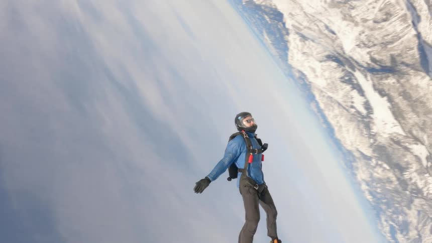 A person with a helmet skydiving with a mountain range the sky and clouds in the background