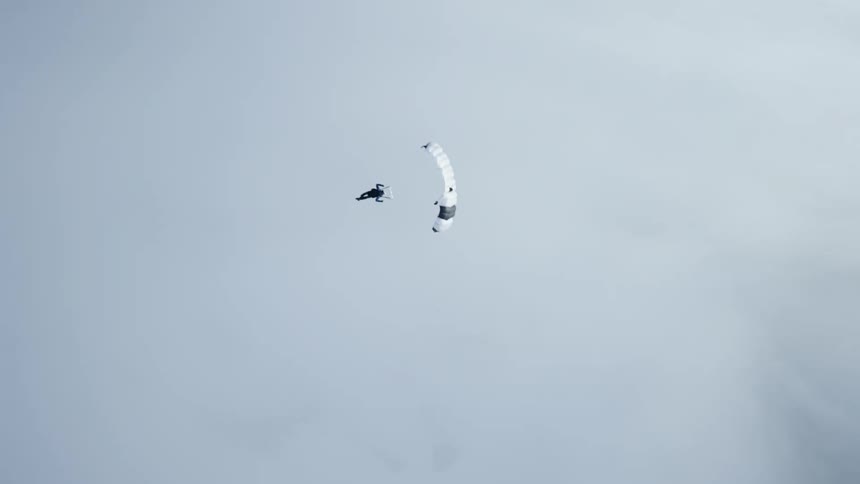 Skydiver wearing a parachute is flying over a snow covered mountain canyon