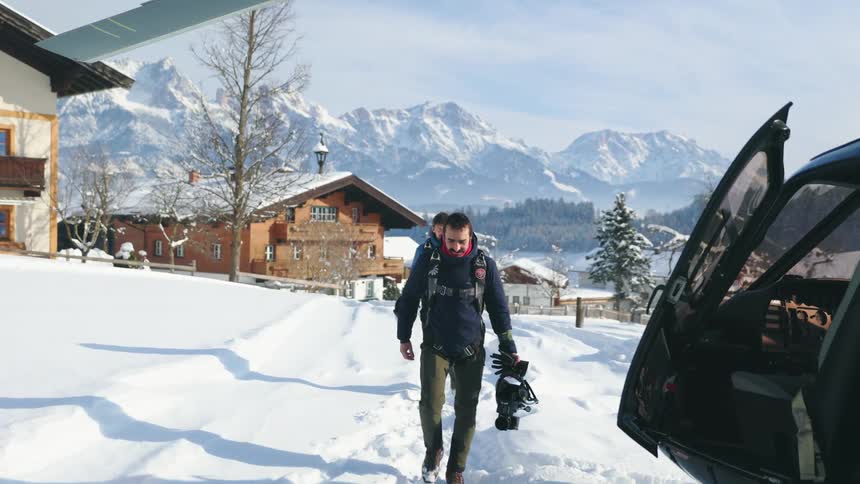 Two men walking towards a helicopter in snowy mountains on a winter day