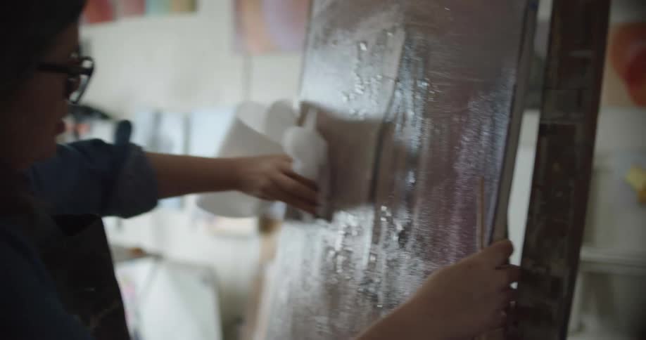 A woman in a room with glasses wiping a canvas with a paper towel