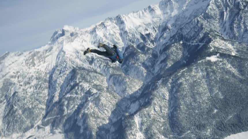 Person wearing a parachute pack is floating over snow covered mountains