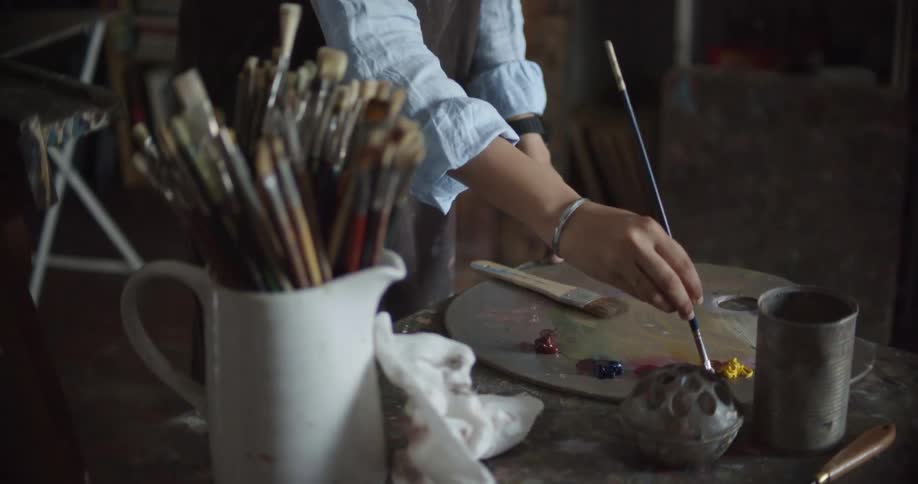 An artist is using a paintbrush to mix paints together on a palette
