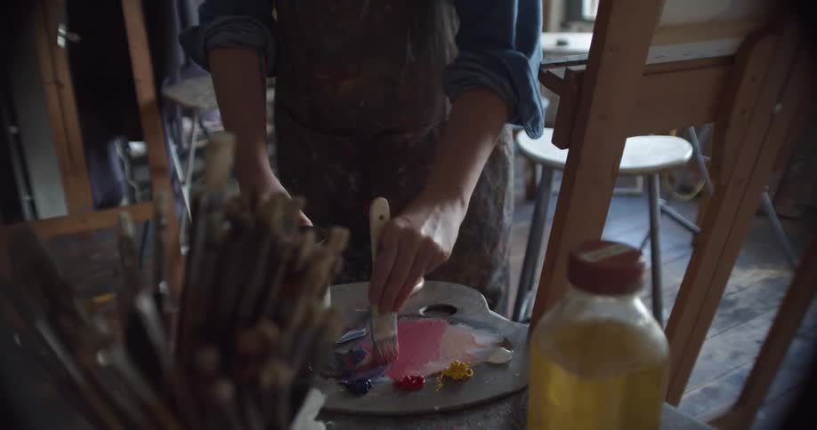 A person in a room mixing paint on a painting pallet with a paint brush