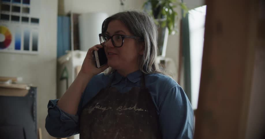 An artist talking on the phone while standing in front of a painting in an art studio