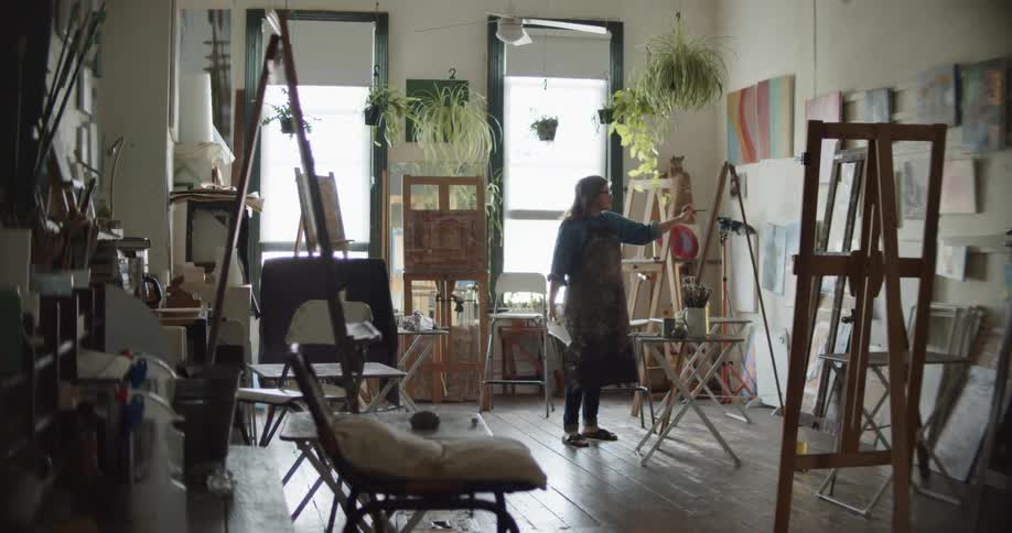 A female painter is painting on a canvas on a painting easel in a studio