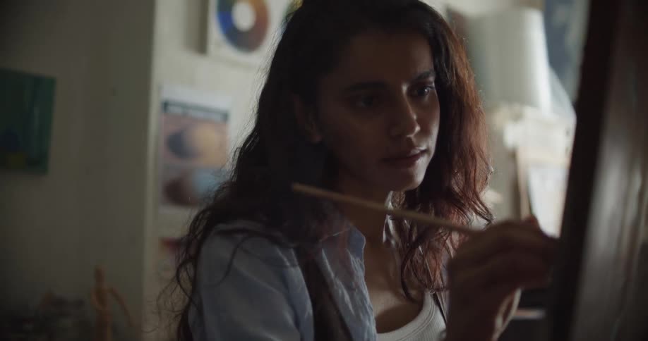 An artist paints on a canvas and then stands back and looks at her work