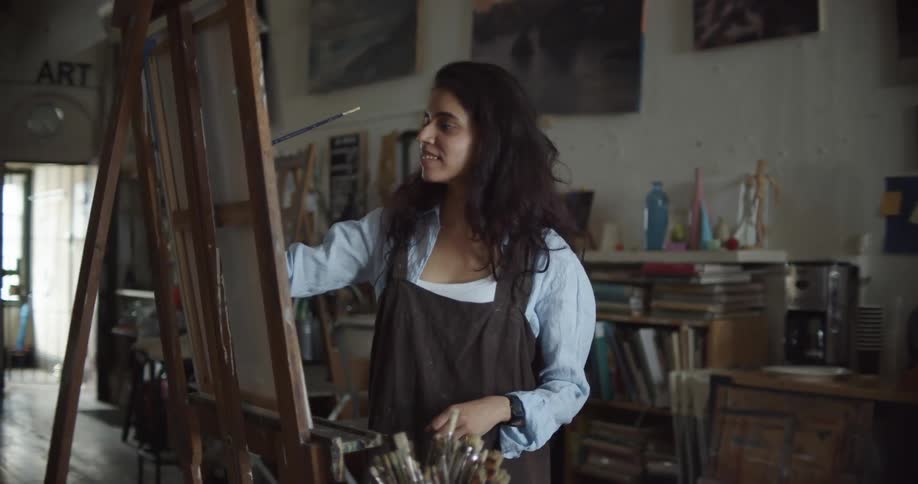 A young woman smiles as she paints on canvas