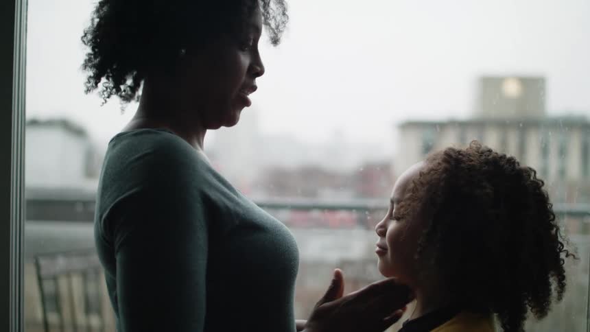 Mother talking th her daughter while caressing her in the face near a window at home
