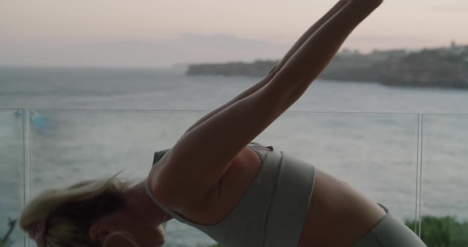 Young fit woman wearing sports clothes working in the balcony near the beach at sunset