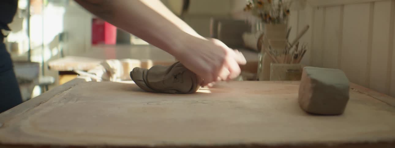 A woman swiftly rolls and presses a medium sized piece of clay in preparation of using it
