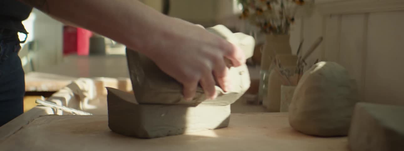 A person placing clay on a table and cutting it with a string
