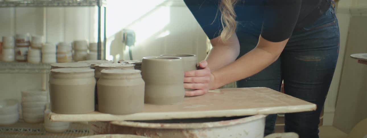 A woman moving clay pottery around in a studio