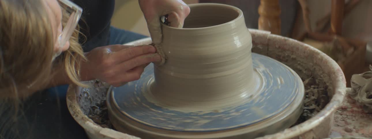 A sculpture shapes clay on a potters wheel in a workshop during the day