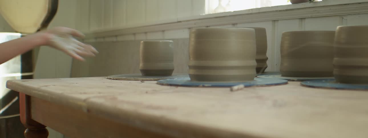 A person setting down a clay pot to dry on a table with other clay pots