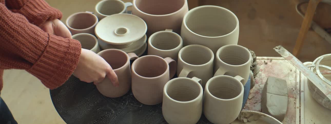 An artist places just made mugs and other pottery on a table