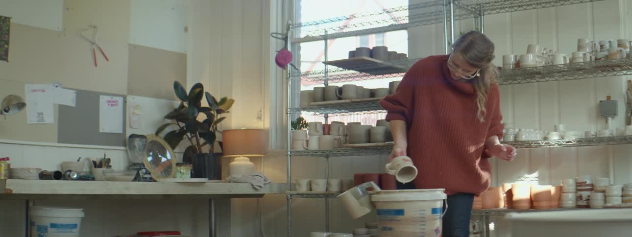 A woman in a sweater creating a mug in a pottery studio