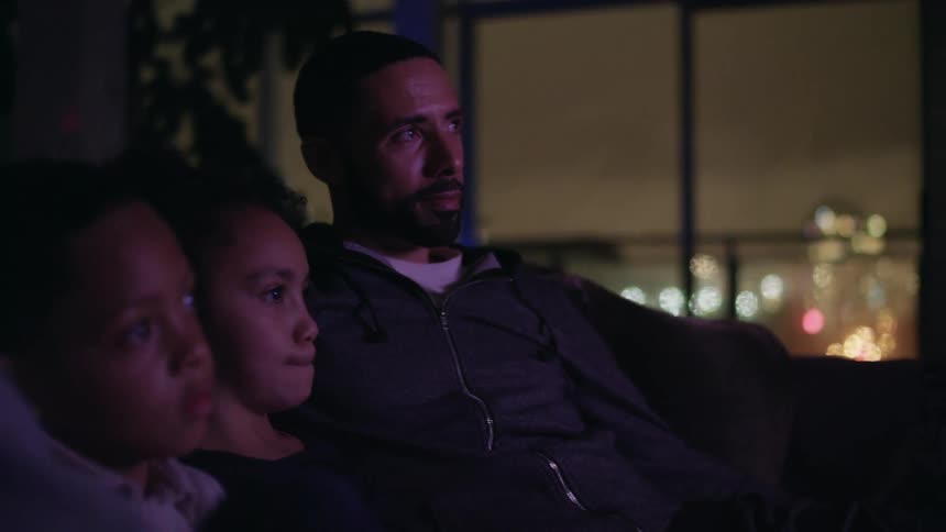 Father watching television with his children siting on a couch in the livingroom at night