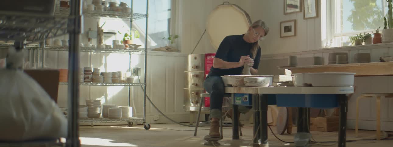 A woman sits at a table and works with clay
