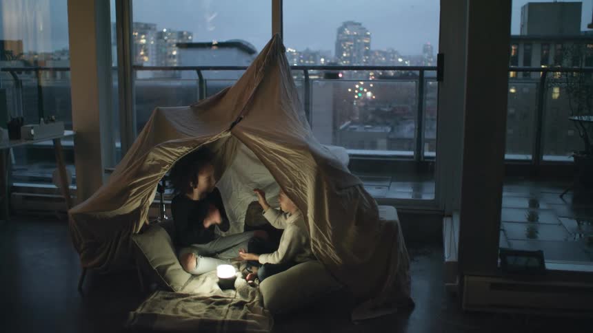 Siblings play a clapping game as they camp indoors in a tent in their downtown condo