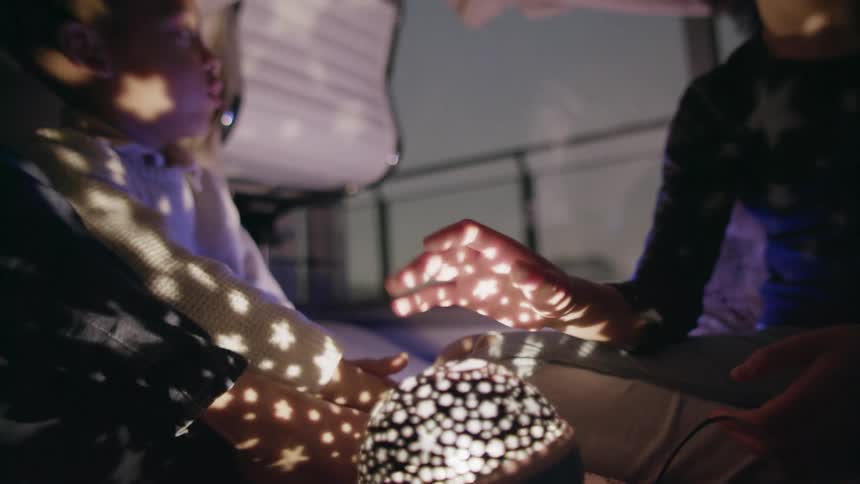 Siblings camp indoors in a tent and play with a led lamp that shines stars on the ceiling