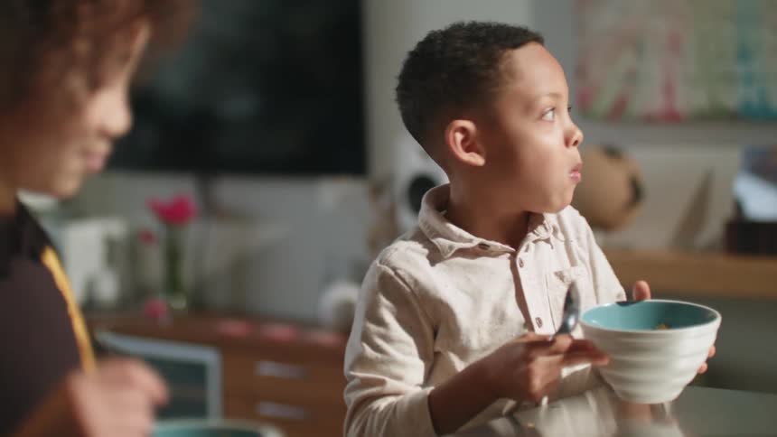 Sister steals cereal from his little brother bowl while he is distracted at breakfast
