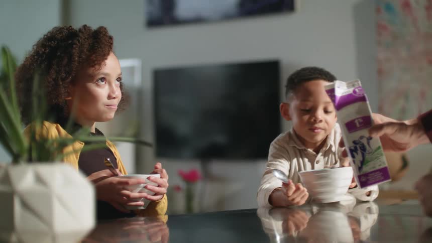 A man pours milk in to bowls of cereal for his children and they eat