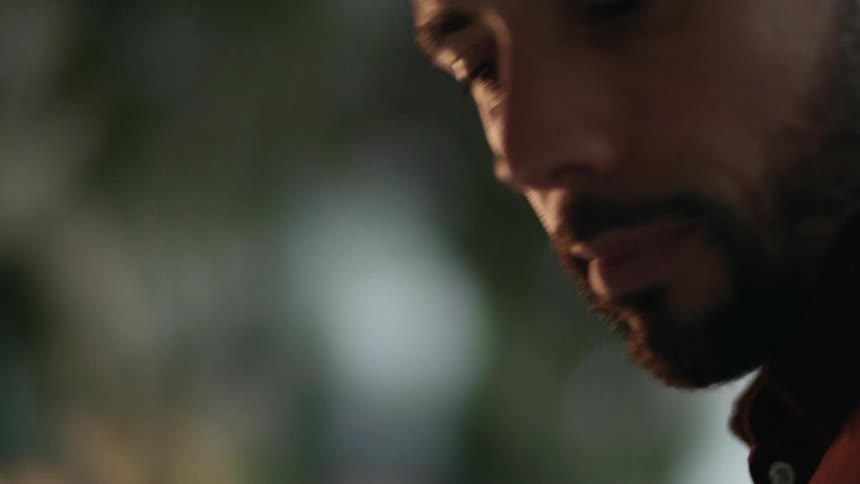 A man in a room looking downward with a window in the background