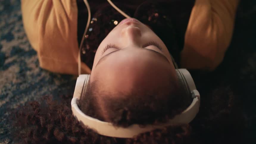 A young girl lays on her back while wearing a pair of large headphones