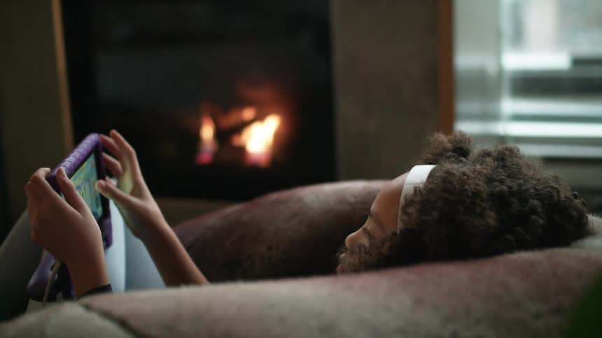 Young girl relaxing next to fireplace playing on a tablet
