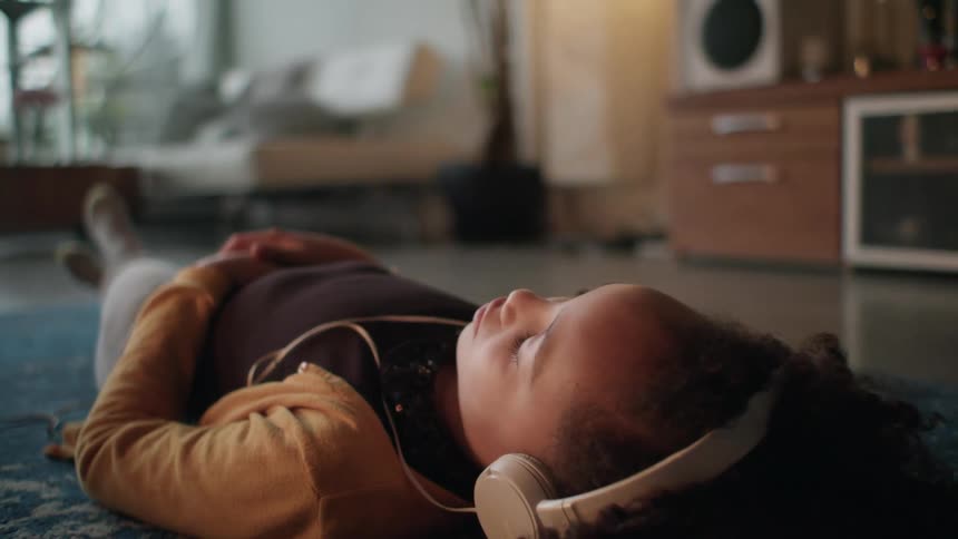 A young girl lays on the floor listening to headphones