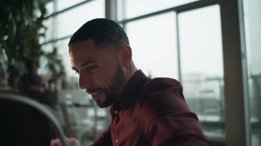 A man is talking to someone while sitting indoors near a window