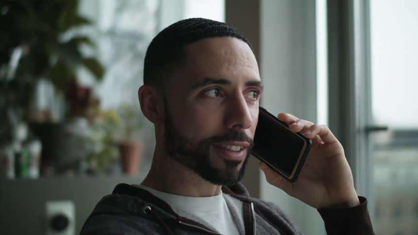 Man talking on a cell phone indoors near a large window