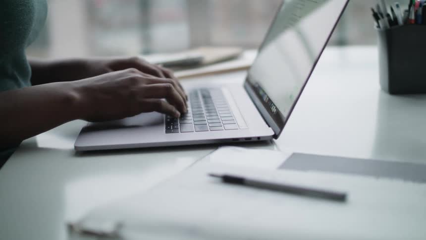 Woman sitting in a desk at her office typing on the keyboard of a laptop near the window