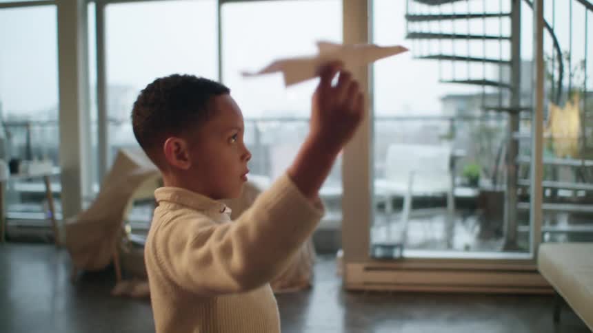 A young boy playing with a paper airplane while standing indoors