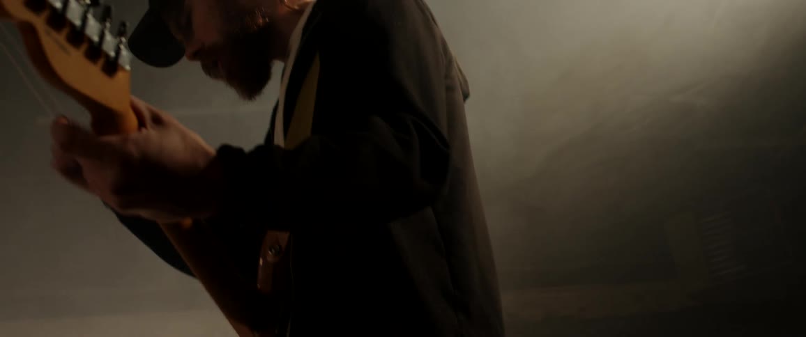 Young man playing electric guitar inside a dimly lit room filled with white smoke