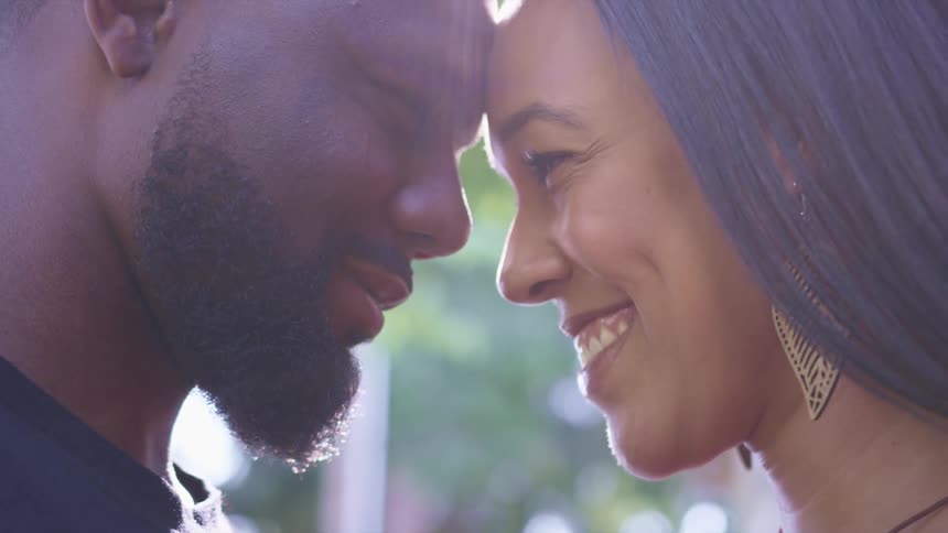 A man and woman touch foreheads and smile as they stand outside