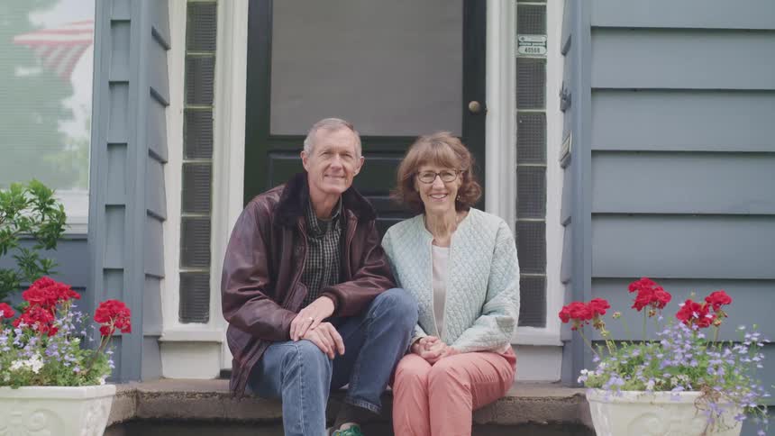 An elderly couple sitting on the step of a front porch on a summer day