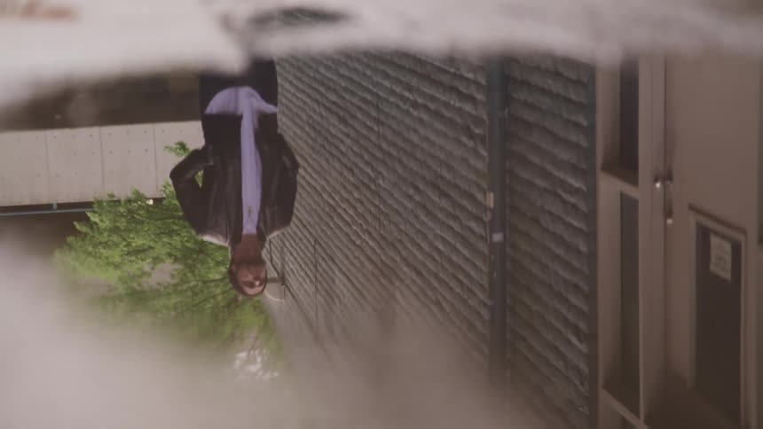 The reflection of a man walking along a sidewalk could be seen in the reflection of puddle water