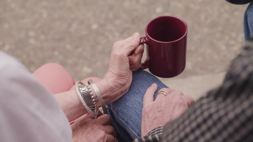 A man and a woman sitting outside holding coffee mugs