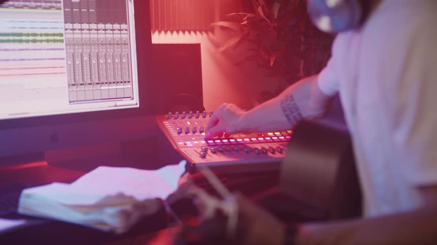 Man recording himself playing acoustic guitar using a console hooked to a computer inside a studio
