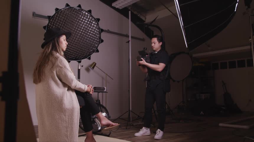 A female model sits on a stool in front of a professional photographer