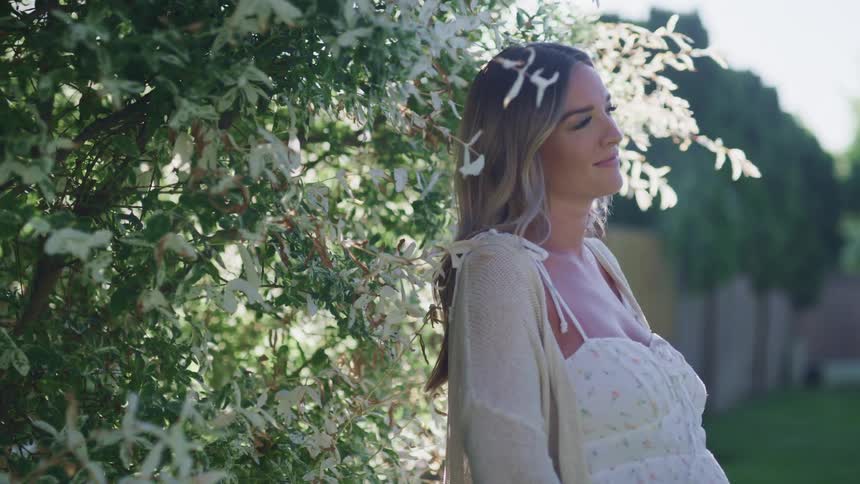 A pregnant woman is standing outdoors by a tree