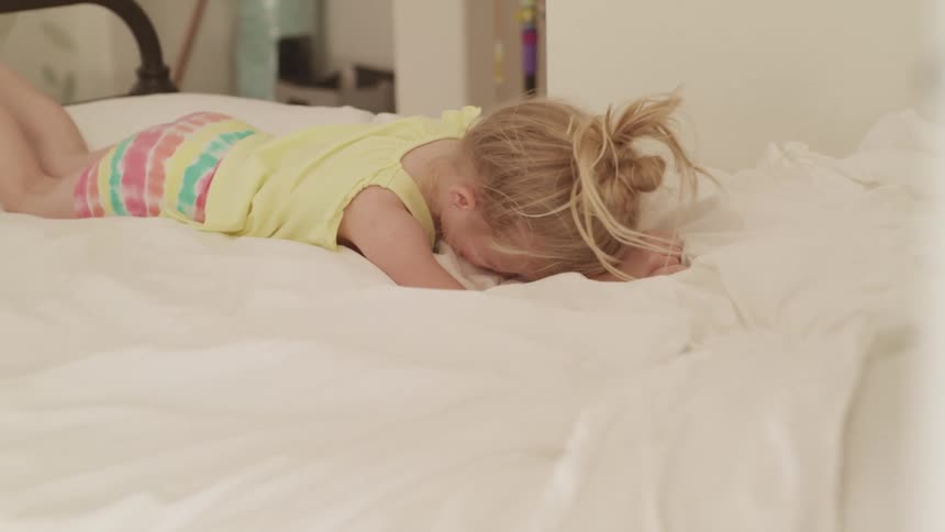 A girl in a bedroom laying on a bed crying with a wall and a doorway in the background
